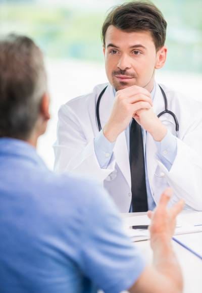Other-Services Male doctor listening attentively to a male patient during a consultation in a bright clinic setting.