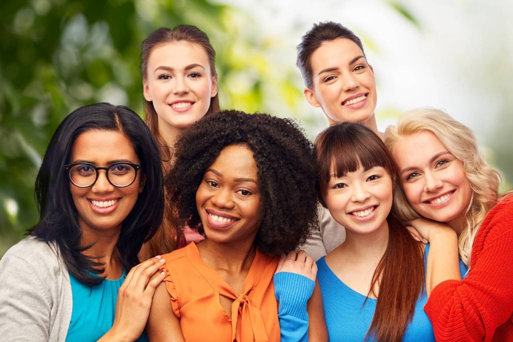 Smiling group of diverse young women standing close together outdoors.