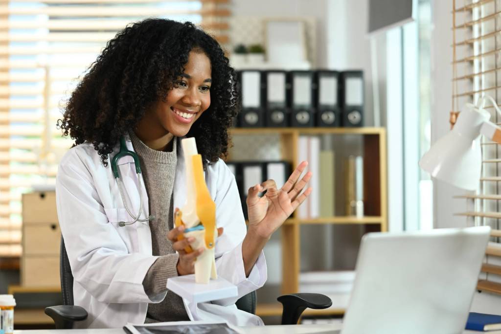 Female doctor providing virtual consultation while explaining a knee joint model.