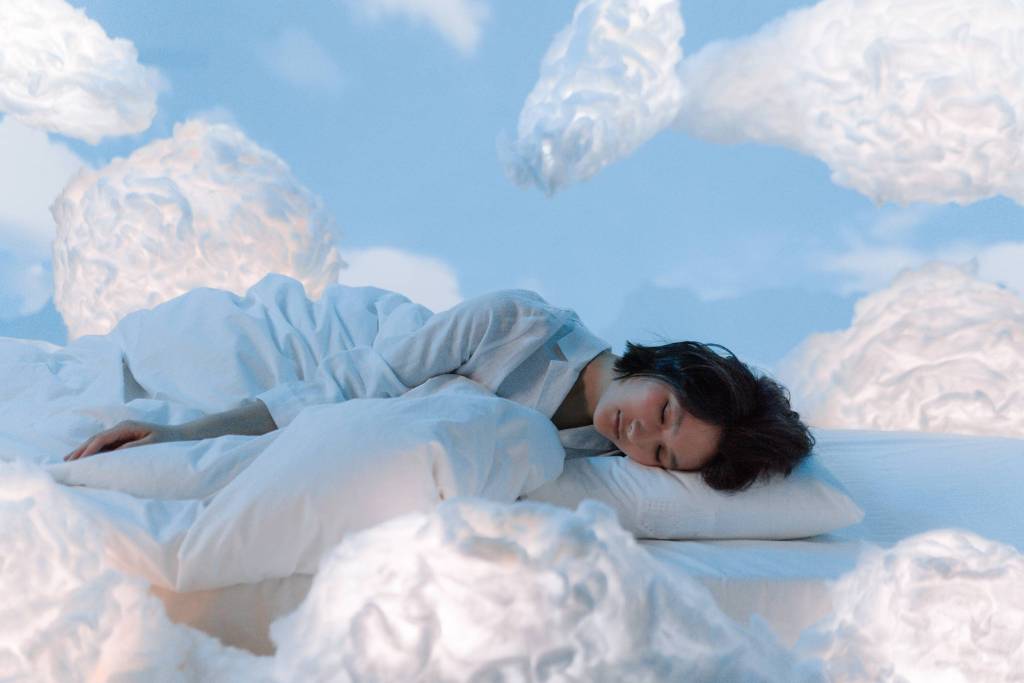 Peaceful woman sleeping in a bed surrounded by clouds in a dreamy sky setting.