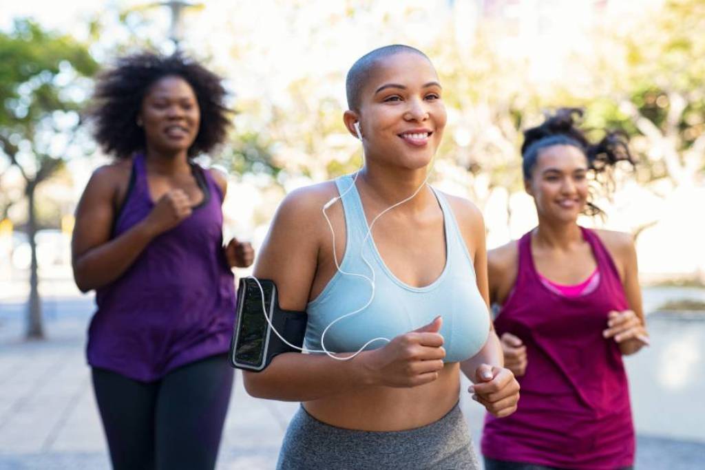Three women jogging outdoors together in athletic wear smiling and enjoying the moment.